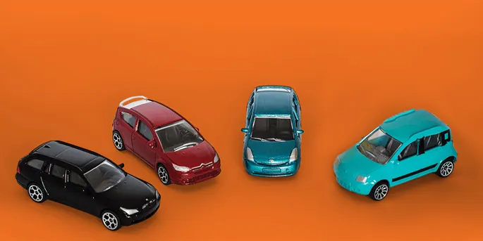 Four toy cars in black, red, blue, and turquoise arranged on an orange background, viewed from above at various angles.