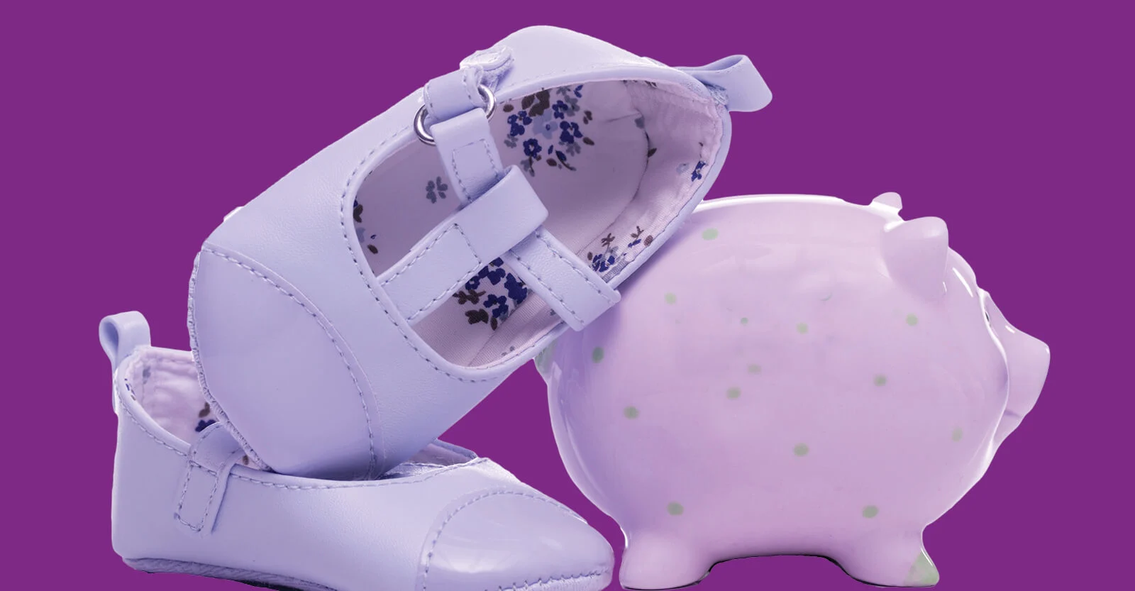 Pair of white baby shoes with floral lining next to a pink polka-dotted piggy bank on a purple background.