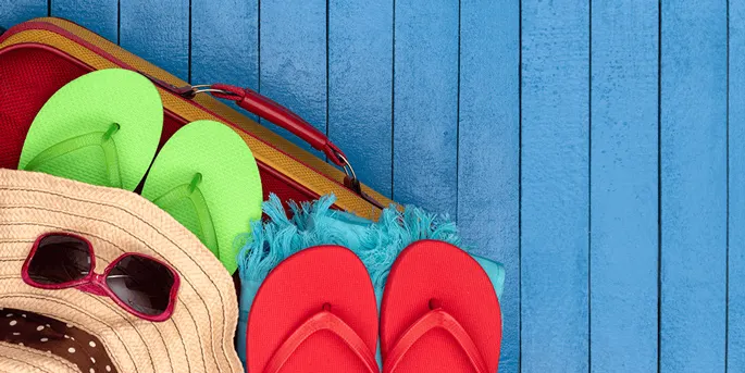 Beach accessories including red and green flip-flops, straw hat, sunglasses, and towel on blue wooden deck