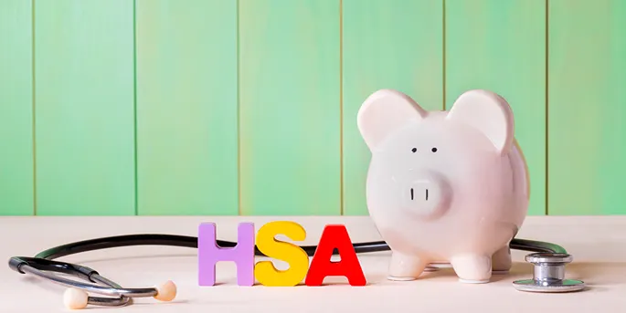 Pink piggy bank with stethoscope and colorful HSA letters on wooden surface against green paneled background