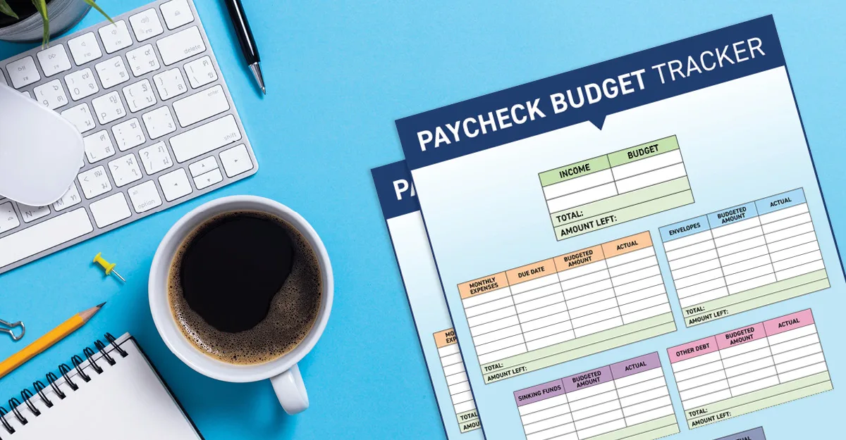 Paycheck budget tracker document on blue desk with keyboard, coffee cup, pen, and office supplies arranged around it.