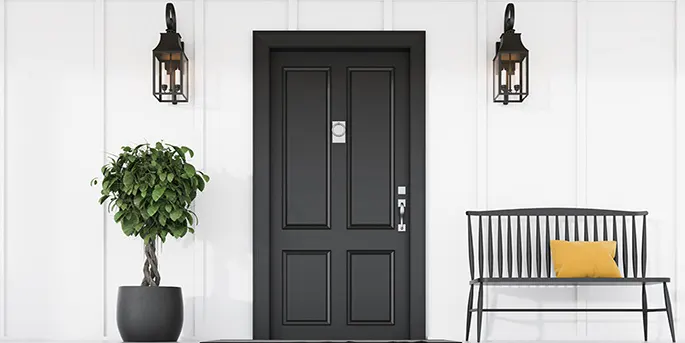 Modern farmhouse entryway with black front door, white paneled walls, lantern sconces, potted topiary, and bench with pillow.