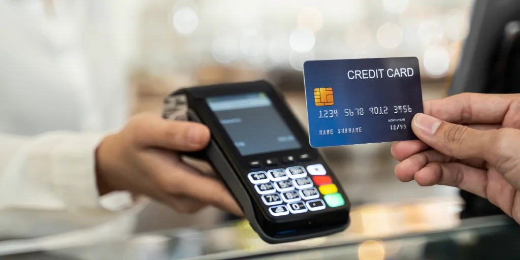 Customer holding blue credit card near payment terminal with cashier operating card reader at checkout counter.