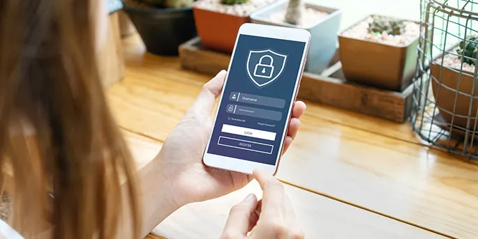 Person holding smartphone displaying security lock icon and login screen on wooden table with plants in background.
