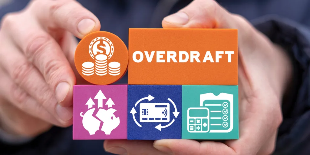 Hands holding colorful blocks with financial icons including coins, piggy bank, credit card, and calculator with OVERDRAFT text