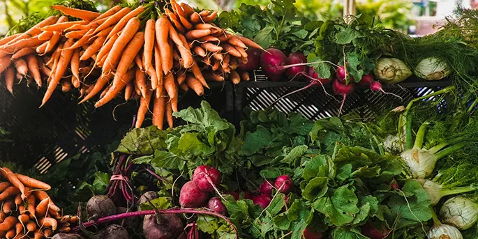 Fresh orange carrots and purple beets with green tops displayed at a farmers market produce stand