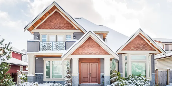 Modern two-story house with brown shingle siding, white trim, gray stone accents, and snow-covered landscaping.