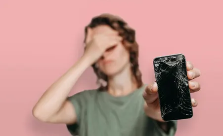 Sad girl holding out her cracked phone on pink background