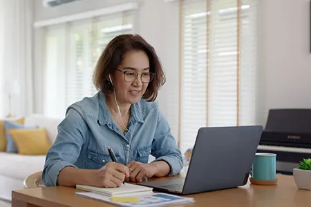 Lady jotting down notes at desk with a laptop