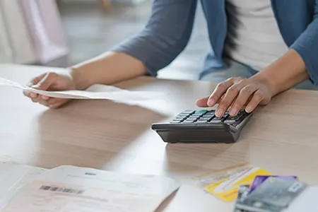 Person using calculator and reviewing documents at desk with papers and money visible