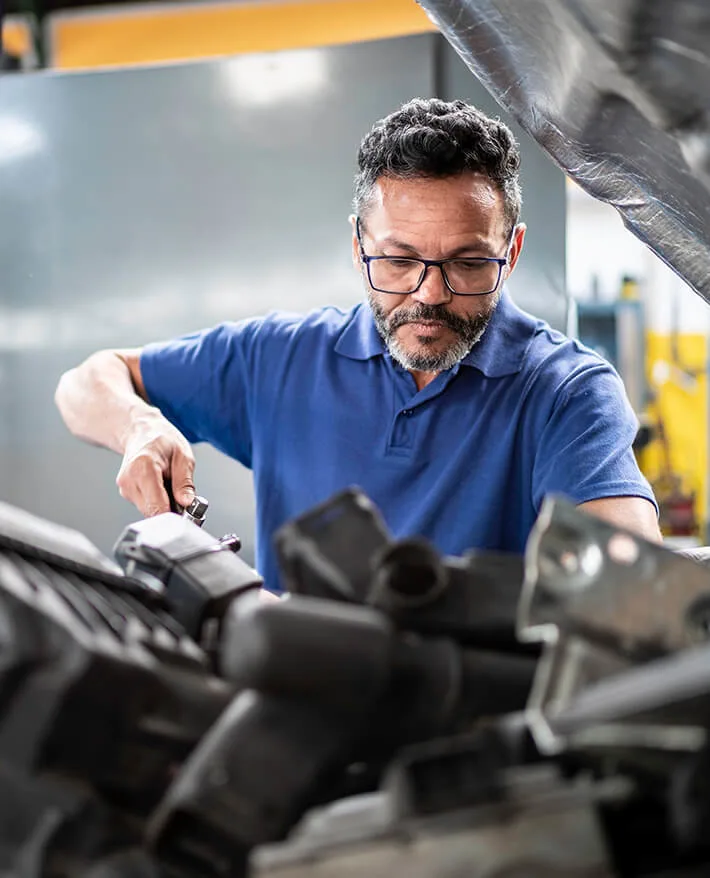 Mechanic in blue shirt and glasses working under car hood in auto repair shop
