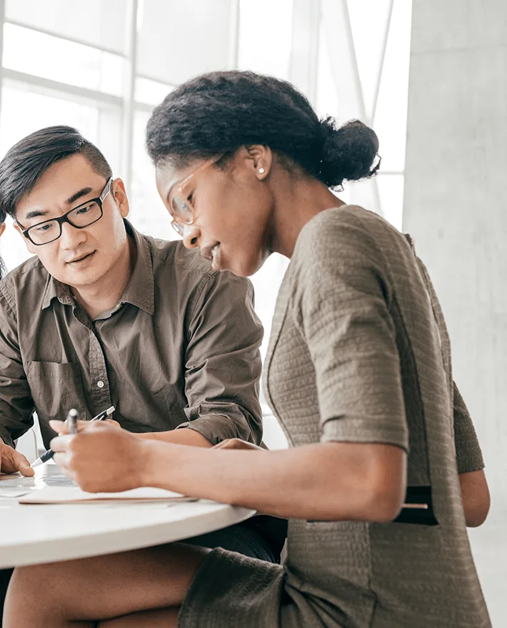 Two professionals collaborating at a desk in a bright office, reviewing documents together in a modern workspace.