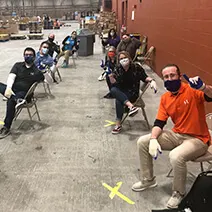 Students and instructor in masks sitting at socially distanced desks in a warehouse-style classroom setting