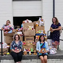 Group of women and children posing with donated food boxes and supplies in front of a garage door