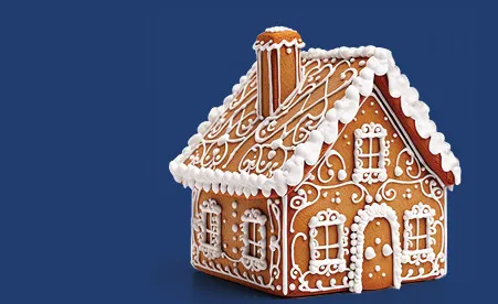 Gingerbread house decorated with white icing, featuring detailed windows, door, and snow-covered roof on blue background.