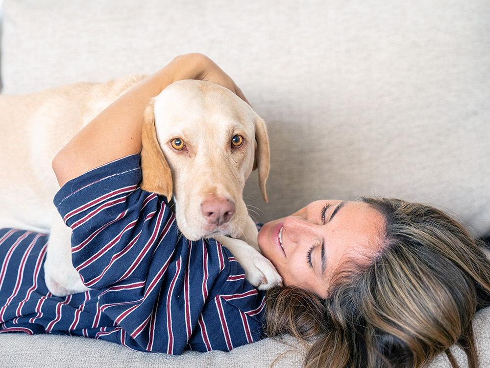 Woman cuddling her dog on the couch at home.