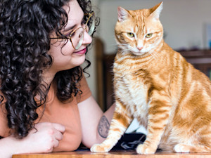 Woman petting her orange cat at home.