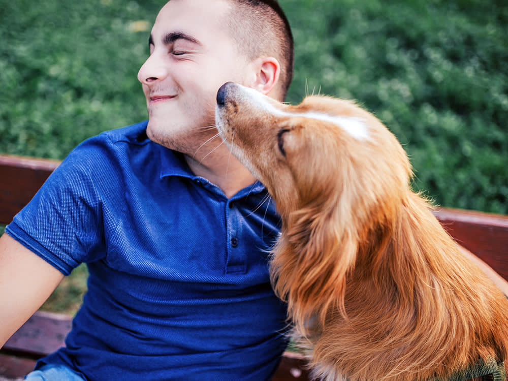 Man leaning away from dog's face outside.