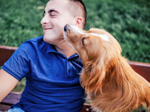 Man leaning away from dog's face outside.