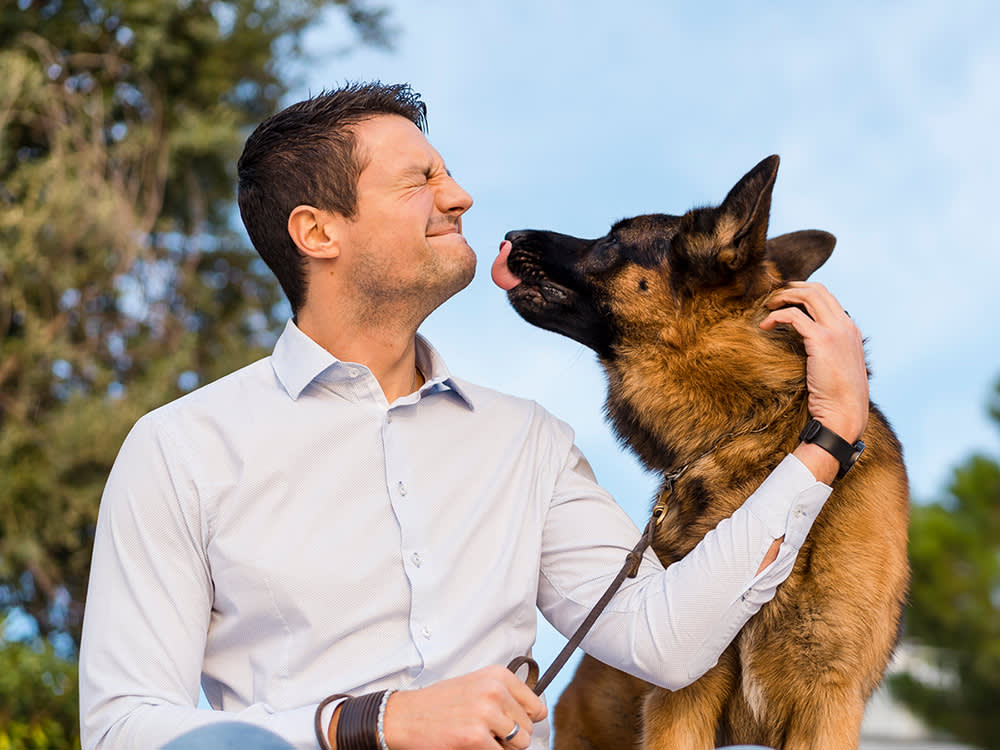 A man with his eyes closed while a dog attempts to lick his face for a kiss.
