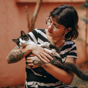 Tattooed and pierced woman wearing a black and white striped shirt and holding an upset looking cat