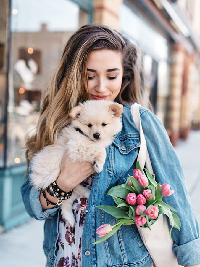 white woman carrying a fluffy dog and a tote of pink tulips