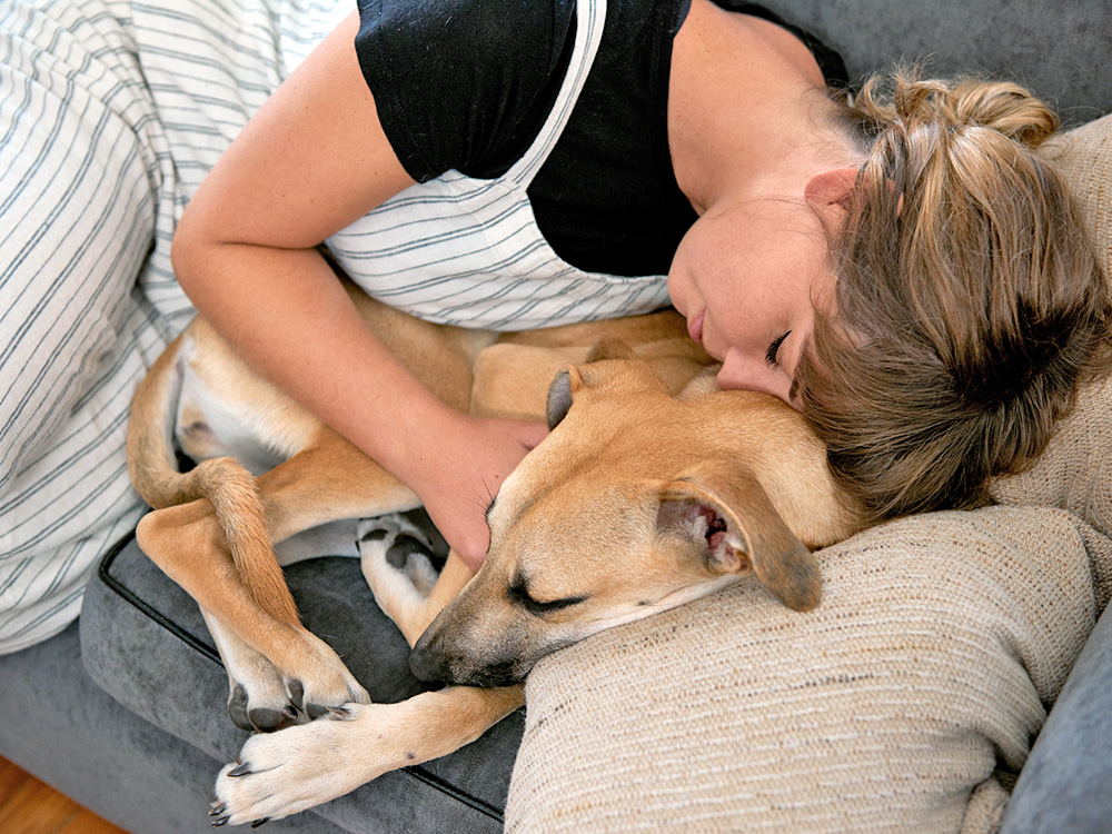 Woman snuggling her dog on the couch at home.