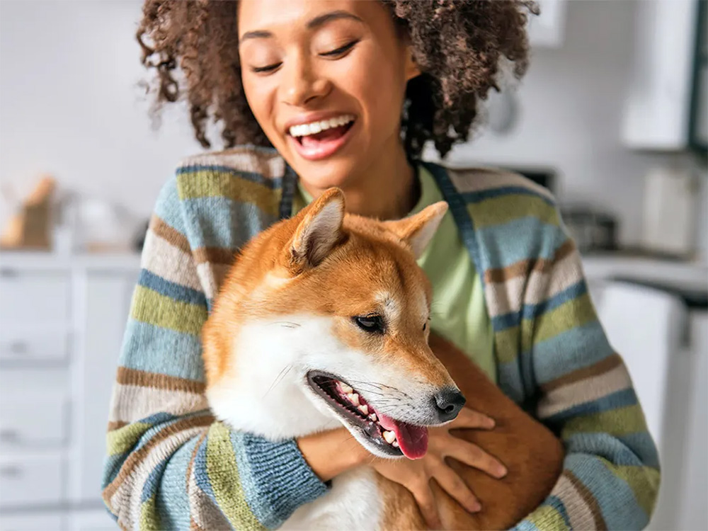 A smiling woman hugs a brown-and-white dog.