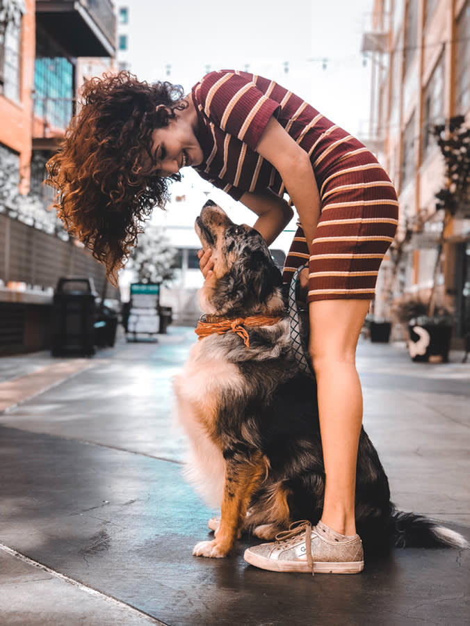 Woman looks down at australian shepherd dog while smiling