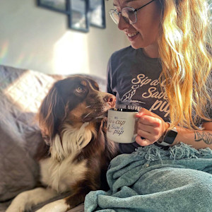 Woman drinking coffee in bed with dog next to her.