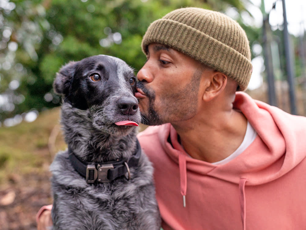 Man kissing his black and white dog outside in the woods.