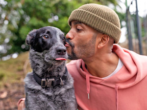 Man kissing his black and white dog outside in the woods.