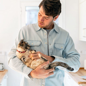 Man cuddling his cat in his arms at home.