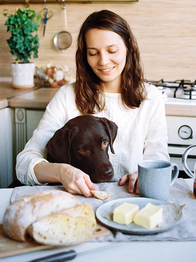 Woman eats garlic bread with her chocolate lab begging nearby.