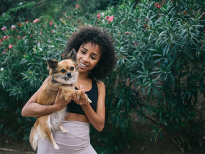Happy young woman in yoga clothes holding small tan dog in park