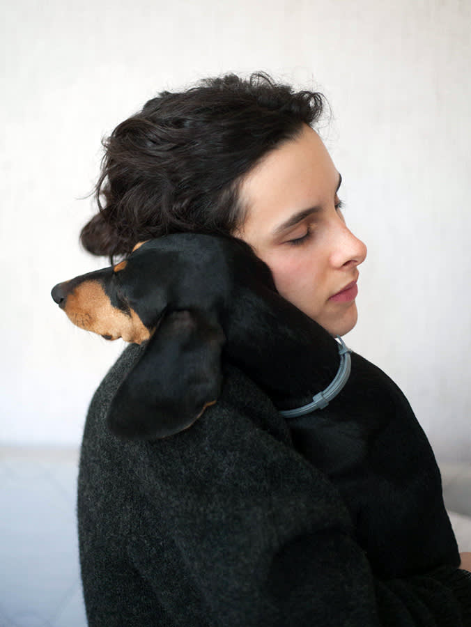 A side profile photograph of a woman with her eyes closed holding her dog in her arms, who is resting their head on her shoulder. 