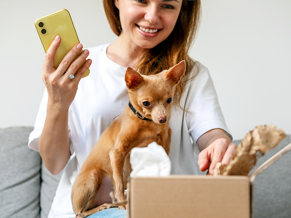 Woman opening a package with her small dog at home.
