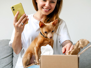 Woman opening a package with her small dog at home.