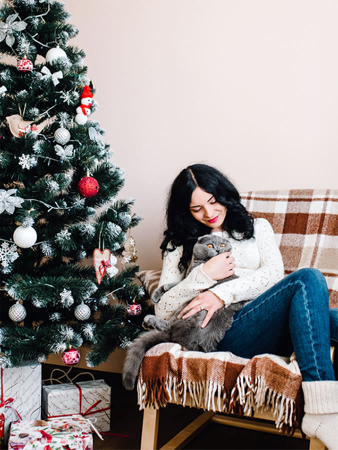 Woman with cat posing near Christmas tree at home.