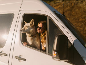 A woman looking out the window of a van with her dog.