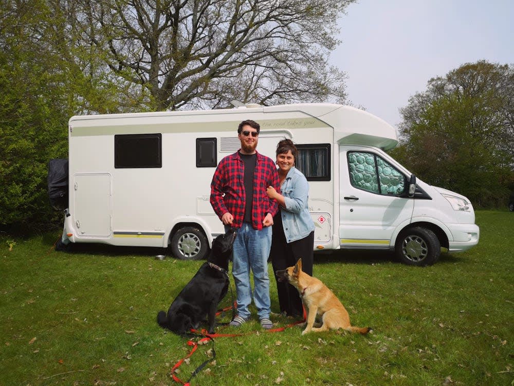 a couple and their two large dogs stand in front of a campervan