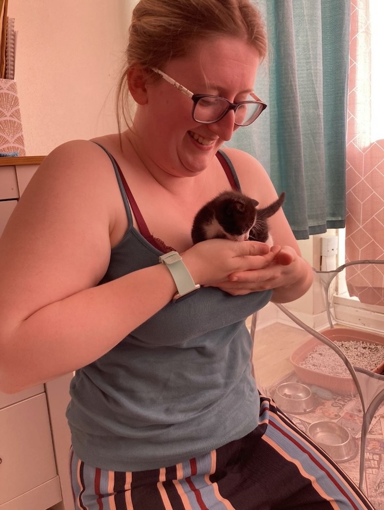 a woman with glasses holds a tiny kitten in her hands