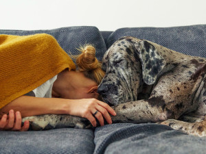 A woman and a dog laying close together on a couch. 