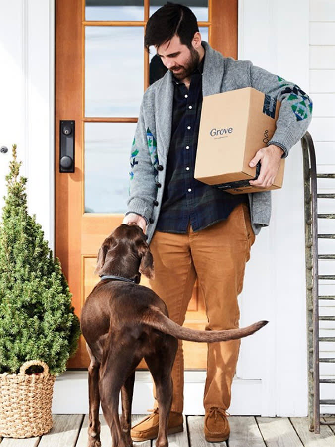 Man holding box while petting dog outside the front door.