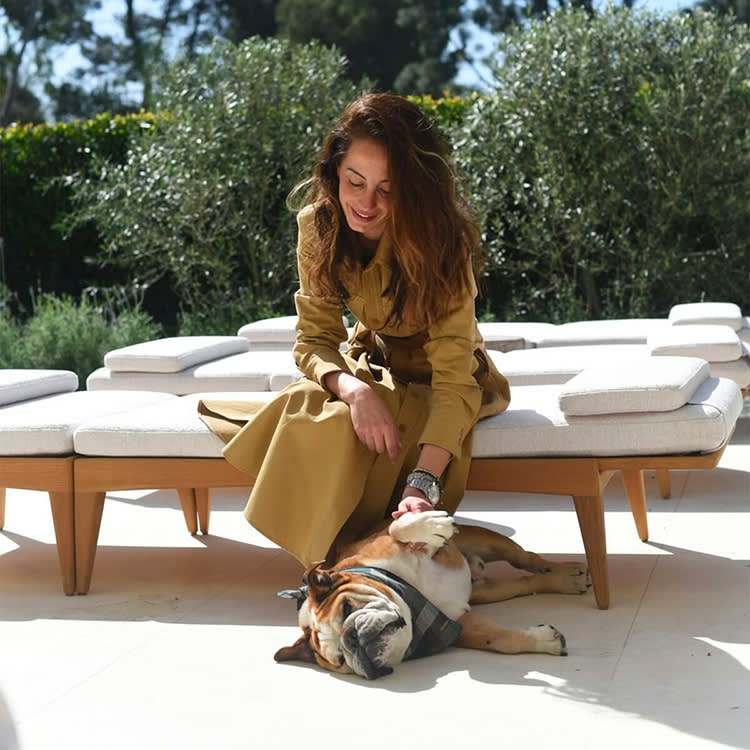 Woman seated on outdoor modern white chairs petting older bulldog laying on its side beneath her