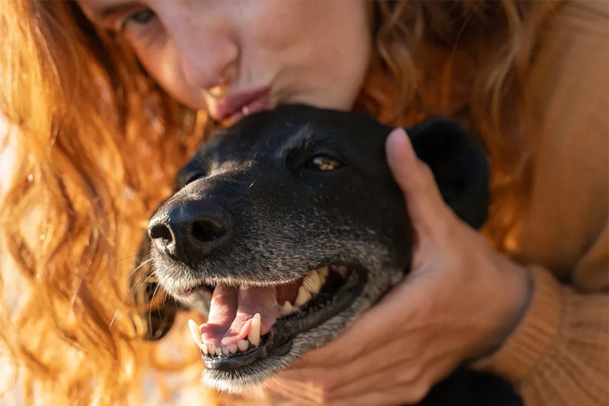 woman kissing dog on top of head while they stick out their tongue