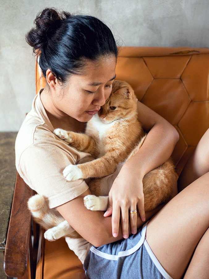 Woman snuggling her orange cat at home.