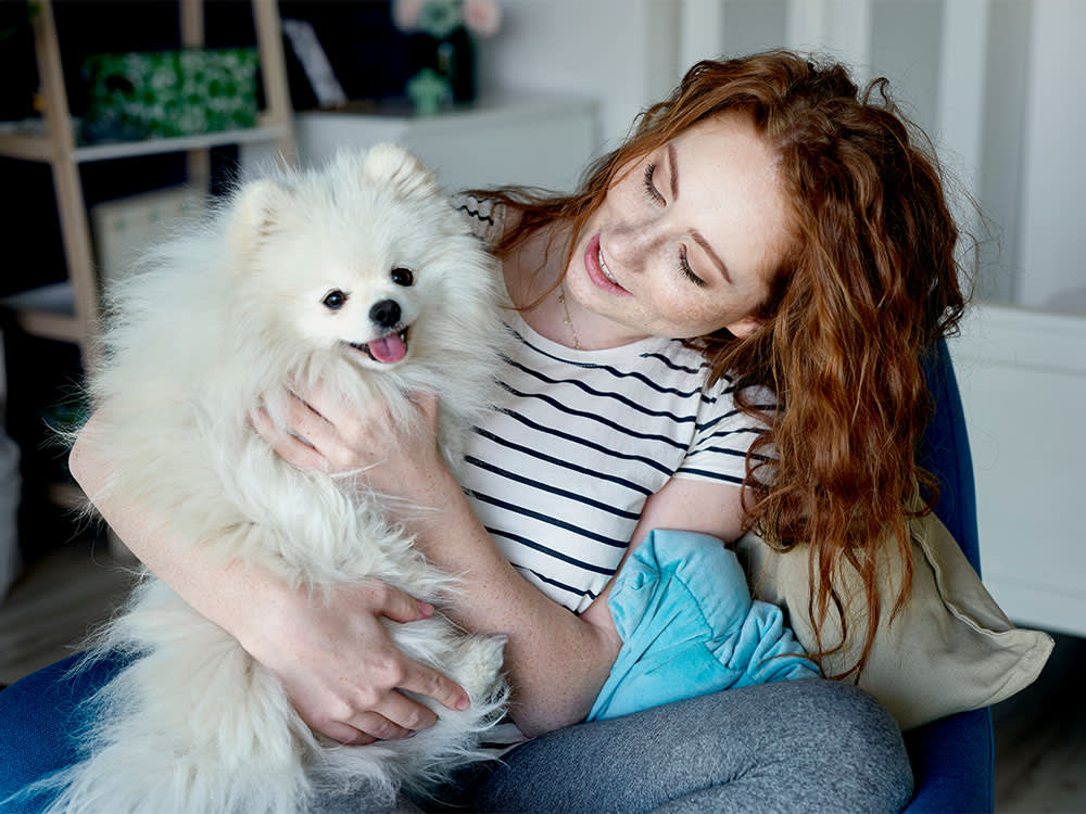 woman with red hair holds senior Pomeranian dog