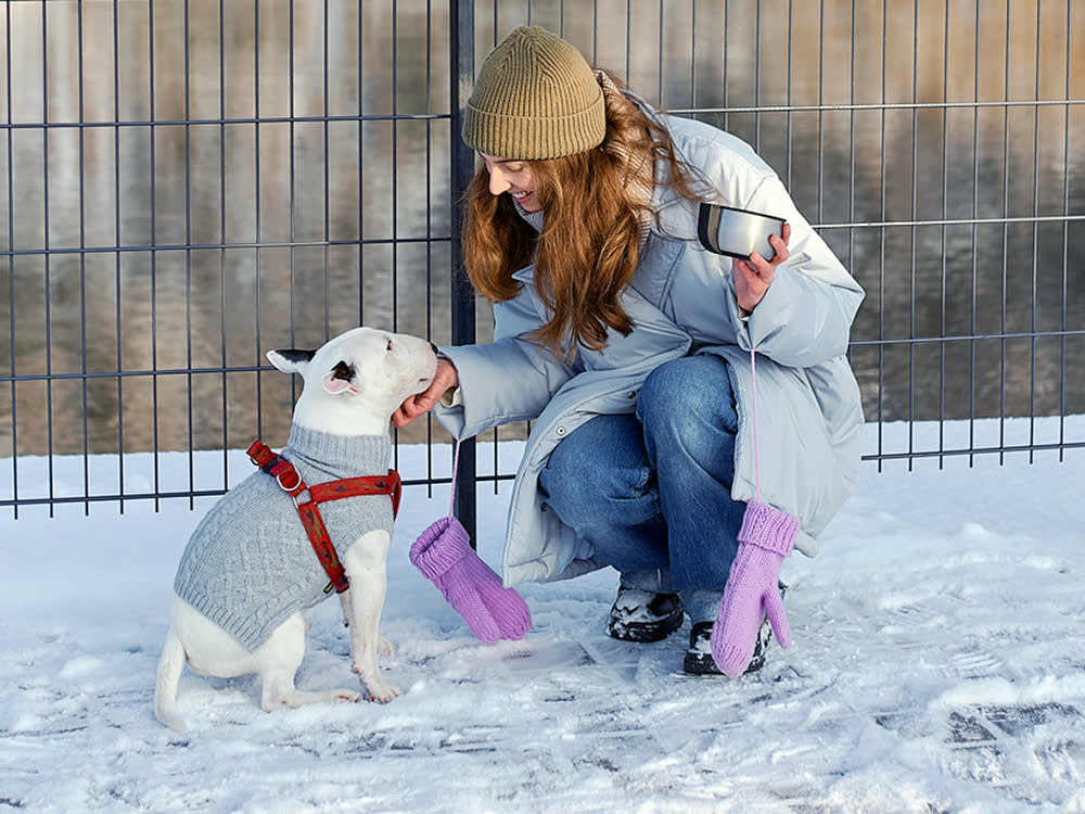 a woman pets her dog in a coat while outside in the snow