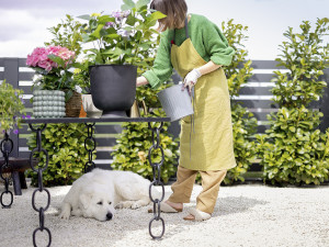 A dog laying under a table outside while a woman cares for her plants. 